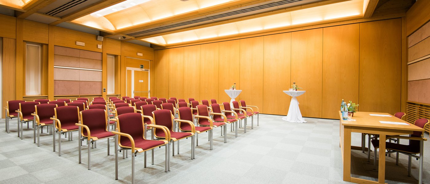 Vermietung Seminarräume Leerer Konferenzraum mit Stühlen, zwei Stehtischen und einem Tisch vorne