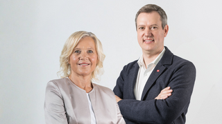 Förderungen und Finanzierungen Porträt von zwei lächelnden Personen mit verschränkten Armen vor weißem Hintergrund