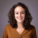 Das lvh-Team Lächelnde junge Frau mit lockigem Haar und braunem Oberteil vor grauem Hintergrund