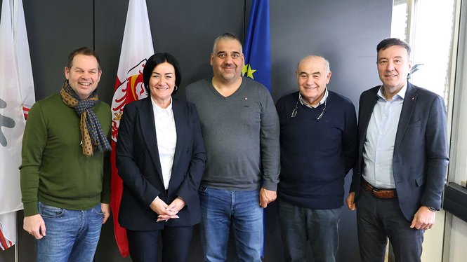 Home Fünf Personen stehen vor Flaggen und lächeln in die Kamera in einem Büro