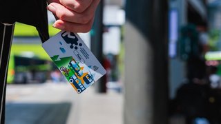 News Hand hält Nahverkehrsticket mit buntem Stadtverkehrsdesign