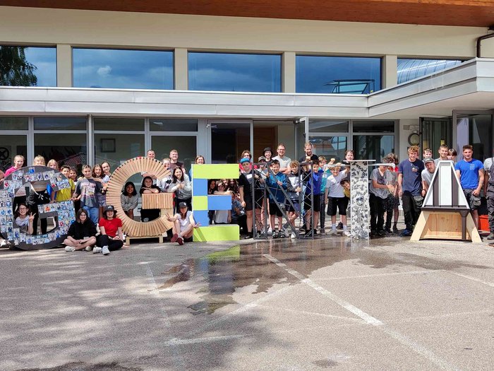 Handwerk hautnah erleben: Schülerinnen und Schüler erkunden vielfältige Berufe und Betriebe im Eggental Große Gruppe von Menschen posiert mit großen Buchstaben vor einem Gebäude