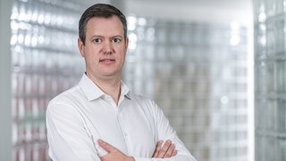 News Uomo con camicia bianca in piedi con le braccia incrociate davanti a parete di vetro