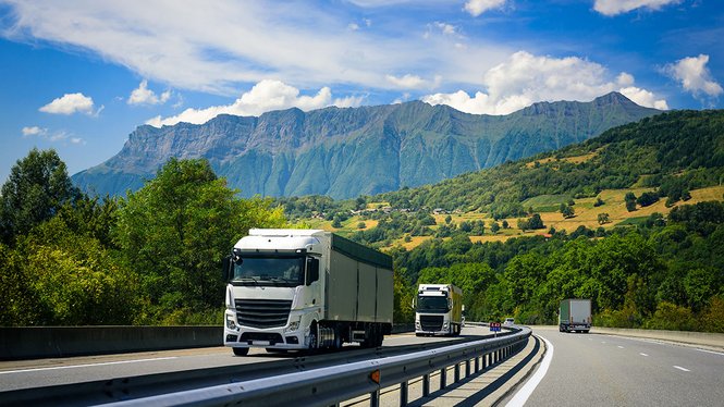 Home LKWs fahren auf Autobahn vor Berglandschaft unter blauem Himmel mit Wolken