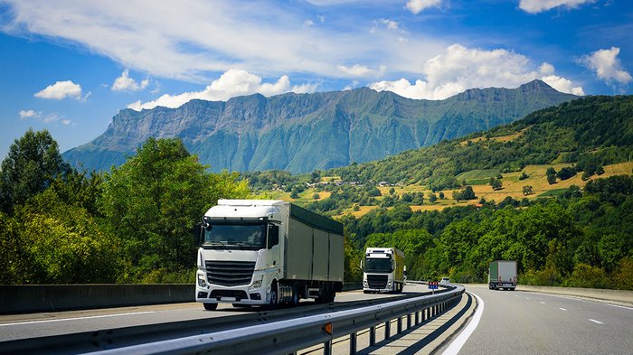 Tag des Kachelofens am 20. Oktober LKWs fahren auf Autobahn vor Berglandschaft unter blauem Himmel mit Wolken