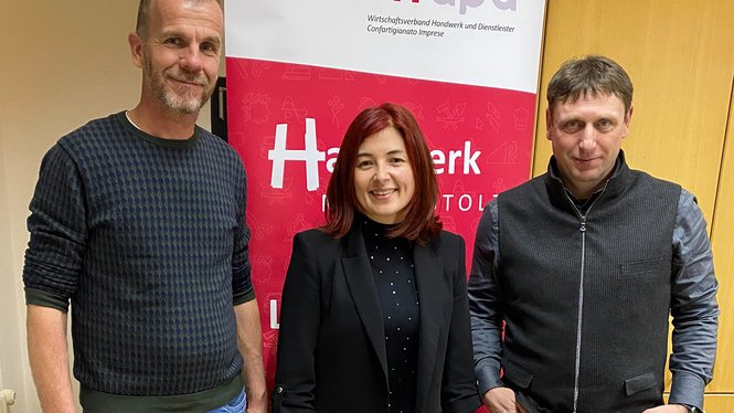 Home Drei Personen stehen vor einem roten Banner mit Handwerkslogo