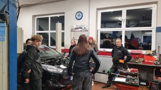 News Gruppe junger Leute in Autowerkstatt beim Gespräch mit Mechaniker vor Auto mit offener Motorhaube