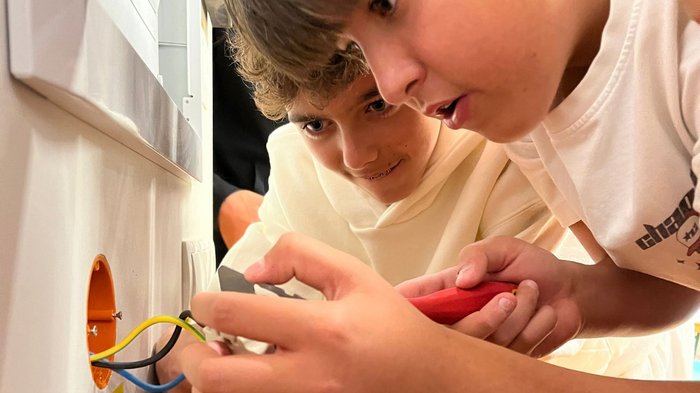 Mittelschule Lana: Berufe praxisnah erleben Zwei Jungen untersuchen bunte Kabel an einer geöffneten Wanddose