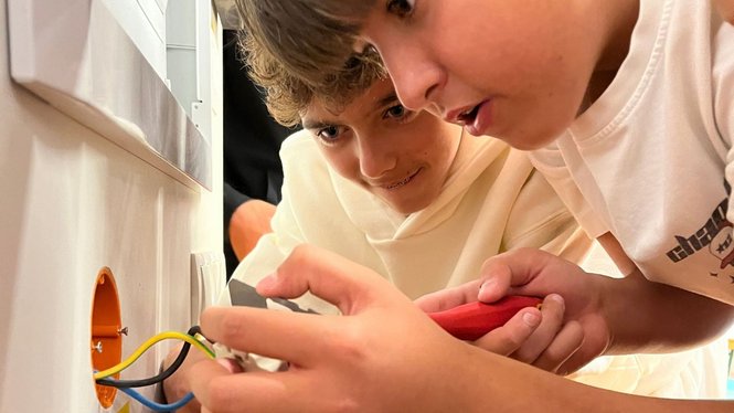 Home Zwei Jungen untersuchen bunte Kabel an einer geöffneten Wanddose