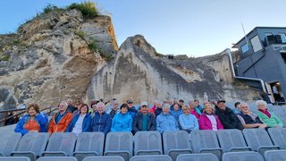 News Anziani seduti su file di sedie davanti a una parete rocciosa in teatro all'aperto