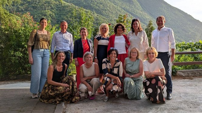 Home Gruppe von elf Personen vor einer bewaldeten Bergkulisse
