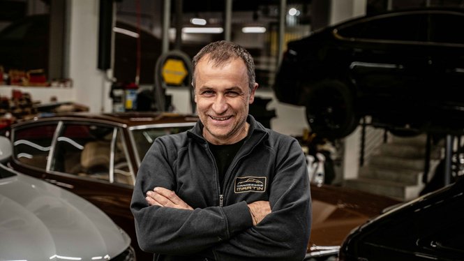 Home Lächelnder Mann mit verschränkten Armen in Autowerkstatt vor mehreren Autos