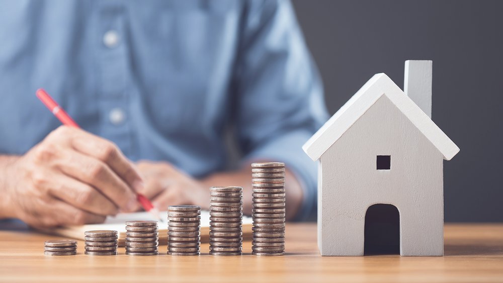 Home Münzstapel wachsen neben einem Modellhaus auf einem Schreibtisch