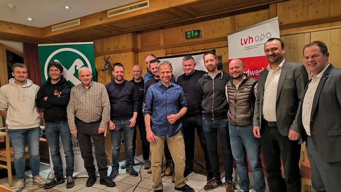 Home Gruppenfoto von zwölf Männern in einem Raum mit Holzverkleidung und Bannern im Hintergrund