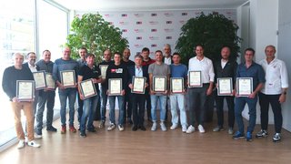 News Gruppo di uomini con certificati in una stanza con piante e logo aziendale sullo sfondo