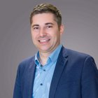 Tirocini in azienda Ritratto di un uomo sorridente con camicia blu e giacca scura su sfondo grigio