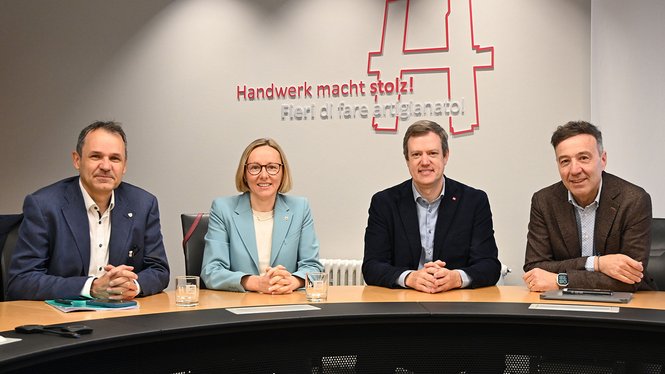 Home Vier Personen sitzen an einem Tisch vor einer Wand mit der Aufschrift Handwerk macht stolz
