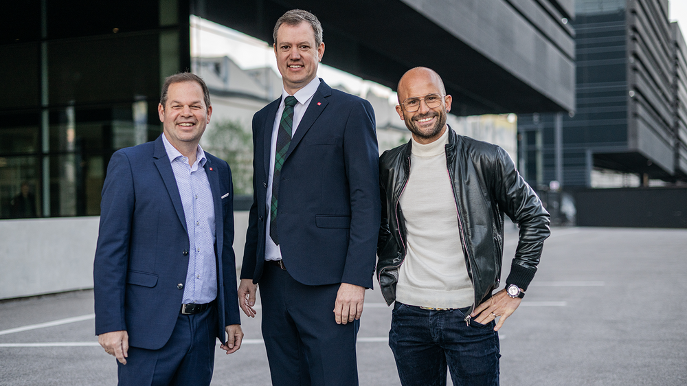 Home Drei Männer stehen lächelnd vor einem modernen Gebäude