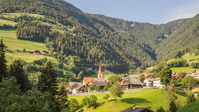 Home Bergdorf mit Kirche in einem grünen, bewaldeten Alpental