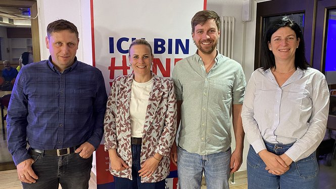 Home Vier Personen vor einem Banner mit der Aufschrift Ich bin Heimat