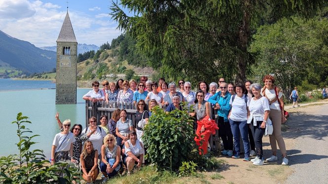 Home Große Gruppe von Menschen vor versunkenem Kirchturm im See bei sonnigem Wetter