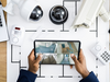 Home Person hält Tablet mit Überwachungskamera-Feeds über einem Tisch mit Sicherheitsausrüstung