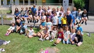 News Foto di gruppo di bambini e un adulto davanti a una scuola professionale al sole