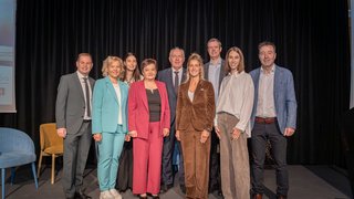 News Nove persone in abbigliamento formale posano su un palco con sfondo nero