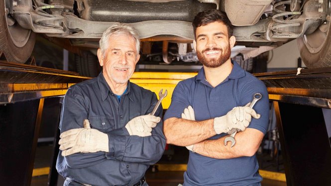 Home Zwei Mechaniker mit Werkzeug unter einem angehobenen Auto in der Werkstatt