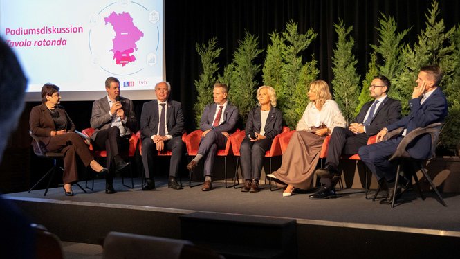 Home Sieben Personen sitzen bei einer Podiumsdiskussion auf einer Bühne