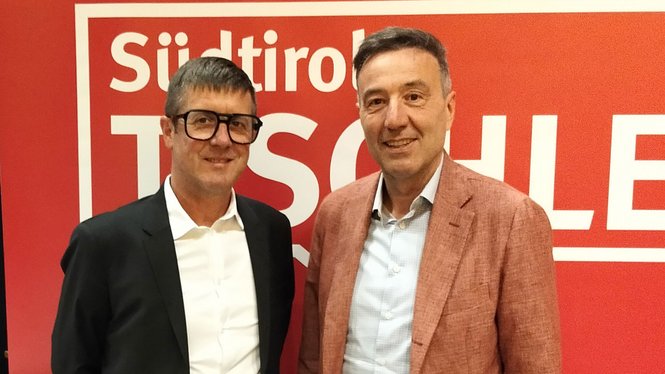 Home Zwei lächelnde Männer vor rotem Hintergrund mit Aufschrift Südtirol