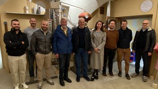 News Gruppo di dieci persone in una stanza con impianto di distillazione sullo sfondo