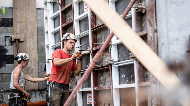 Home Zwei Bauarbeiter mit Helmen arbeiten an einer Betonwand mit Werkzeugen