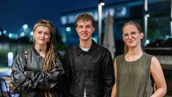 Home Drei Personen posieren bei einer Abendveranstaltung vor einem beleuchteten Gebäude
