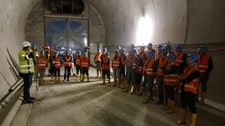 News Gruppo di operai con caschi e giubbotti riflettenti in galleria durante istruzioni