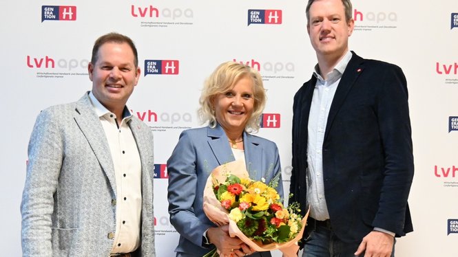Home Drei Personen lächeln, eine mit Blumenstrauß vor lvhapa-Hintergrund