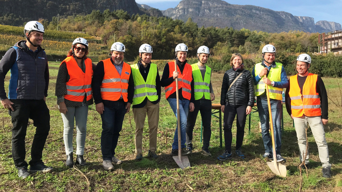 Home Gruppe von neun Personen mit Helmen und Warnwesten auf einem Feld vor Bergen
