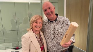 News Due persone sorridenti in ufficio, una tiene un blocco note, l'altra un cilindro