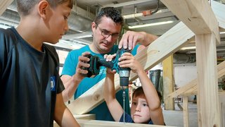 News Mann hilft Jungen beim Bohren in Holzrahmen in einer Werkstatt