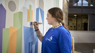 News Junge Frau malt bunte geometrische Formen an eine Wand