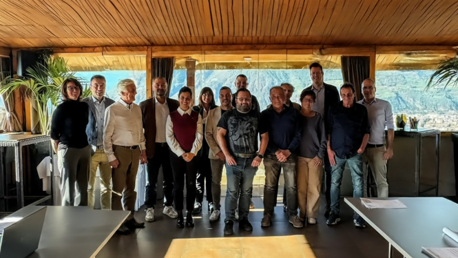 Home Gruppenfoto von 14 Personen in einem Raum mit großen Fenstern und Bergblick