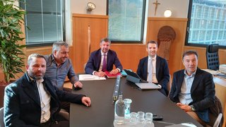 News Fünf Männer in Anzügen sitzen an einem Konferenztisch in einem Büro