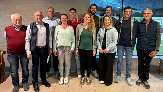 Home Gruppenfoto von elf Personen vor einer grauen Wand im Innenraum