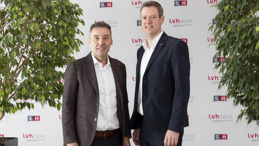 Home Zwei Männer im Anzug stehen vor einer lvhapa gesponserten Wand zwischen zwei Pflanzen