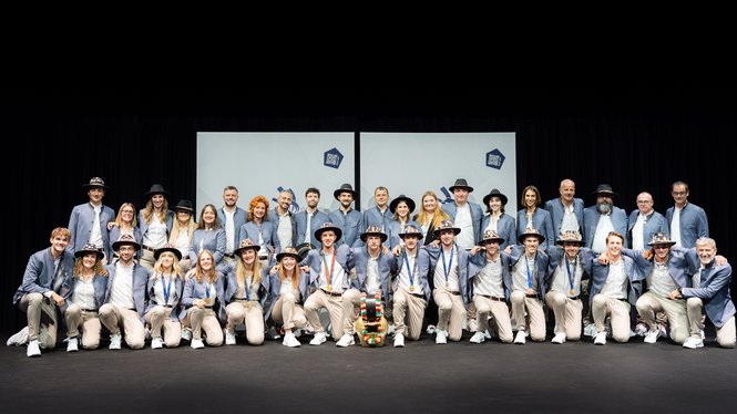 Home Gruppe in blauen Jacken und Hüten auf einer Bühne vor hellen Leinwänden