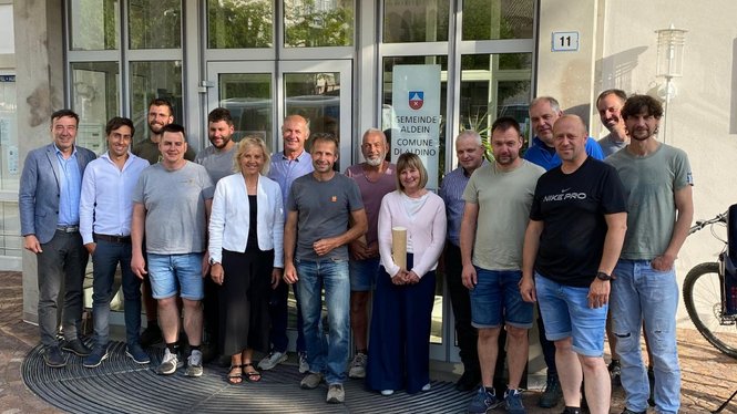 Home Gruppenfoto von 16 Personen vor dem Eingang des Gemeindehauses Aldein