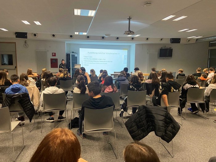 Mittelschule Klausen: Traumberufe in Gastgewerbe, Handwerk, Handel und Dienstleistungen vorgestellt Schulklasse hört zu bei einer Präsentation über Schuster-Ausbildung in einem Klassenzimmer.