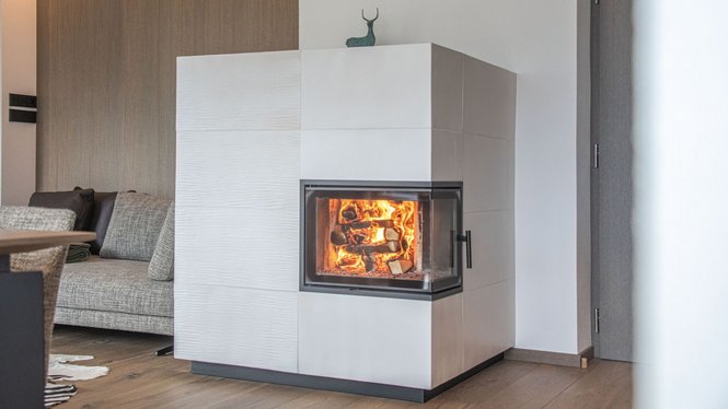 Home Weißer Kaminofen mit loderndem Feuer neben einem grauen Sofa im Wohnzimmer