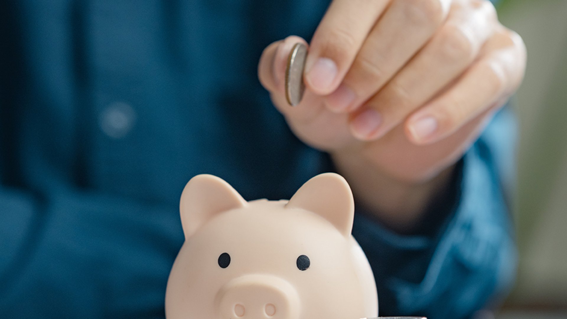 Home Person wirft Münze in Sparschwein neben Münzstapeln auf Schreibtisch