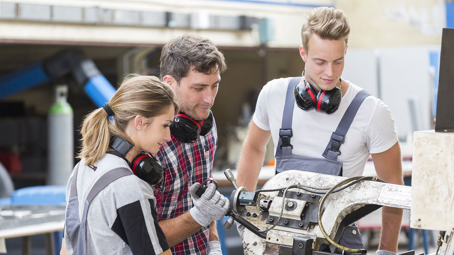 Home Drei Auszubildende arbeiten mit einer Metallmaschine in einer Werkstatt